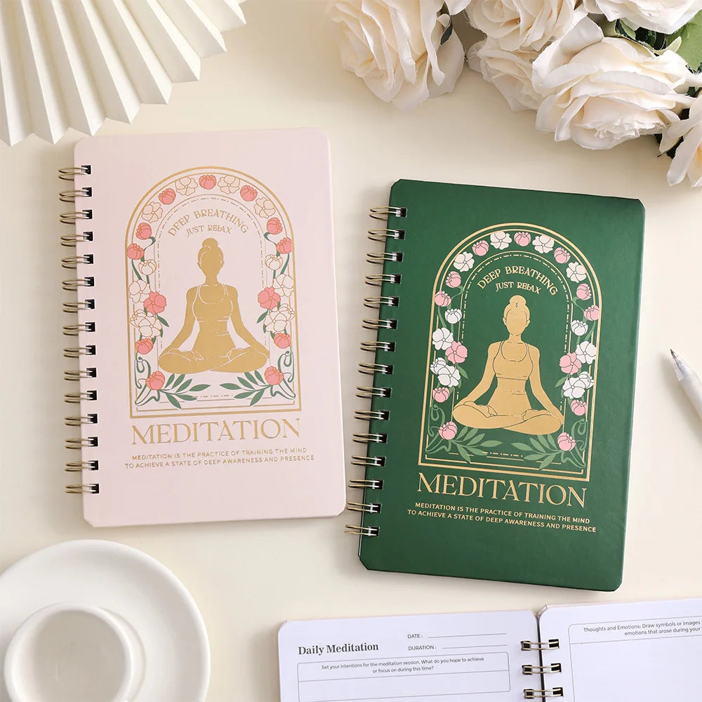 Two spiral-bound meditation notebooks, one pink and one green, on a light surface with flowers in the background, for mindfulness and mental health