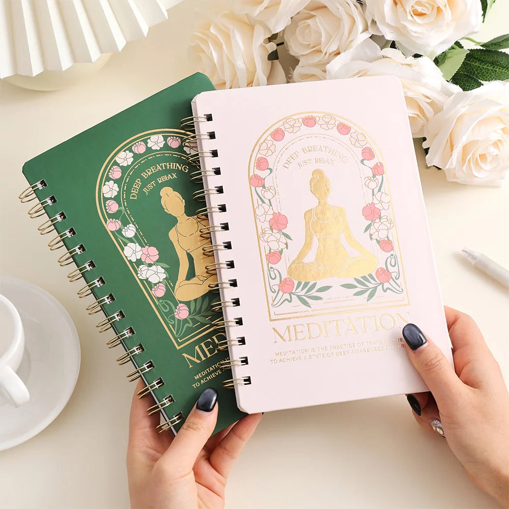 Two spiral-bound notebooks with decorative covers featuring a Buddha illustration on a table with flowers and a cup, for mindfulness meditation and mental health