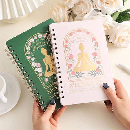Two spiral-bound notebooks with decorative covers featuring a Buddha illustration on a table with flowers and a cup, for mindfulness meditation and mental health